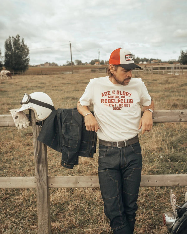 Baffle Haus off-white 100% cotton Wild Ones graphic tee worn by a man leaning on a wooden fence in a rural setting.
