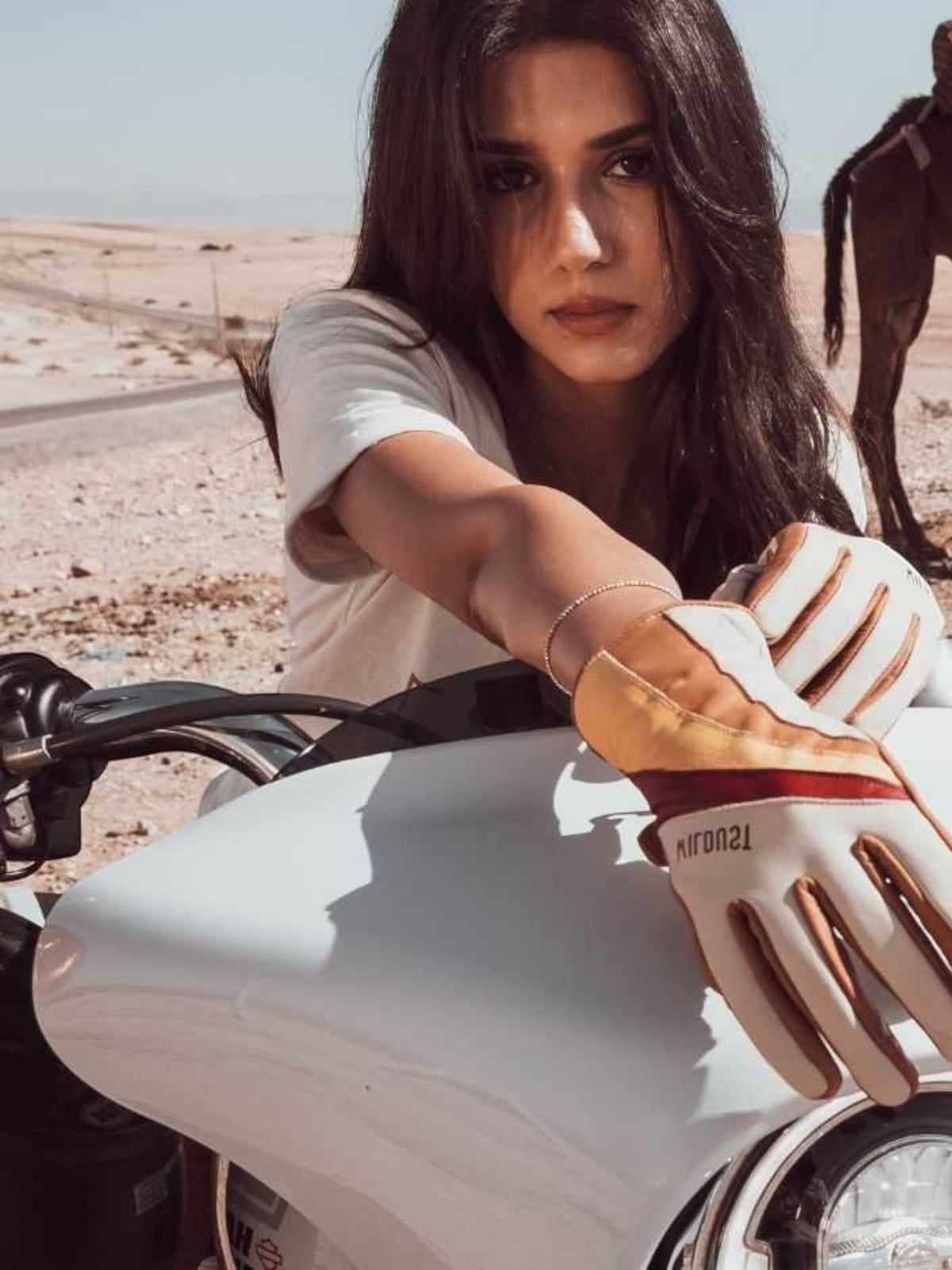 Baffle Haus Wildust 70s stripe leather motorcycle gloves in white and red worn by a woman on a white motorcycle