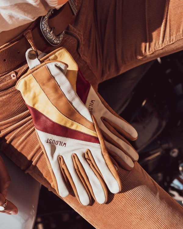 Baffle Haus Wildust 70s stripe leather motorcycle gloves in white, yellow, and red resting on corduroy trousers