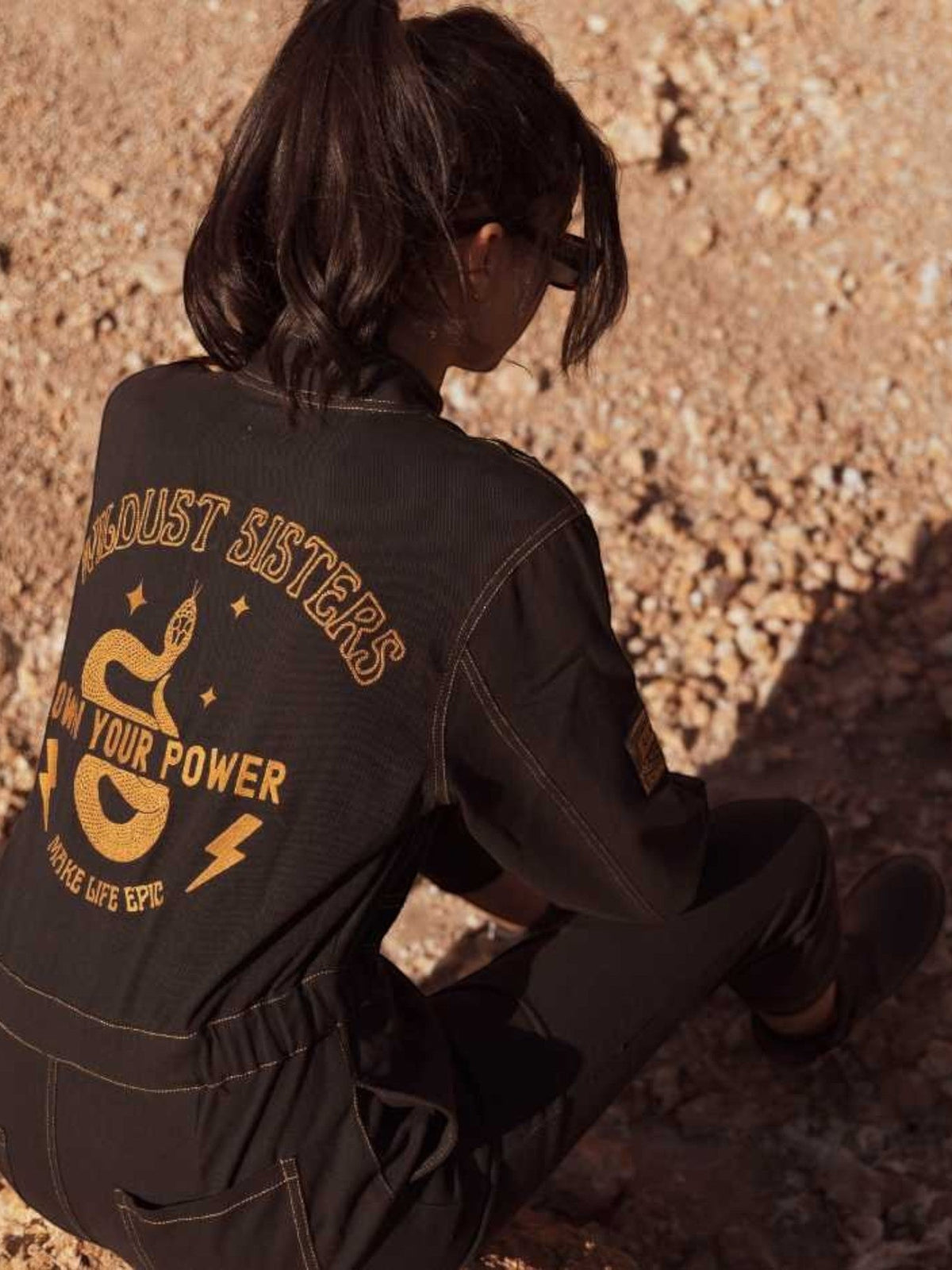 Baffle Haus Wildust black cotton aviator jumpsuit with Own Your Power snake embroidery on the back, outdoor setting