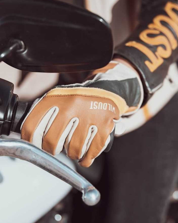 Baffle Haus Wildust 70s stripe motorcycle gloves in camel and green leather worn on a motorcycle handlebar