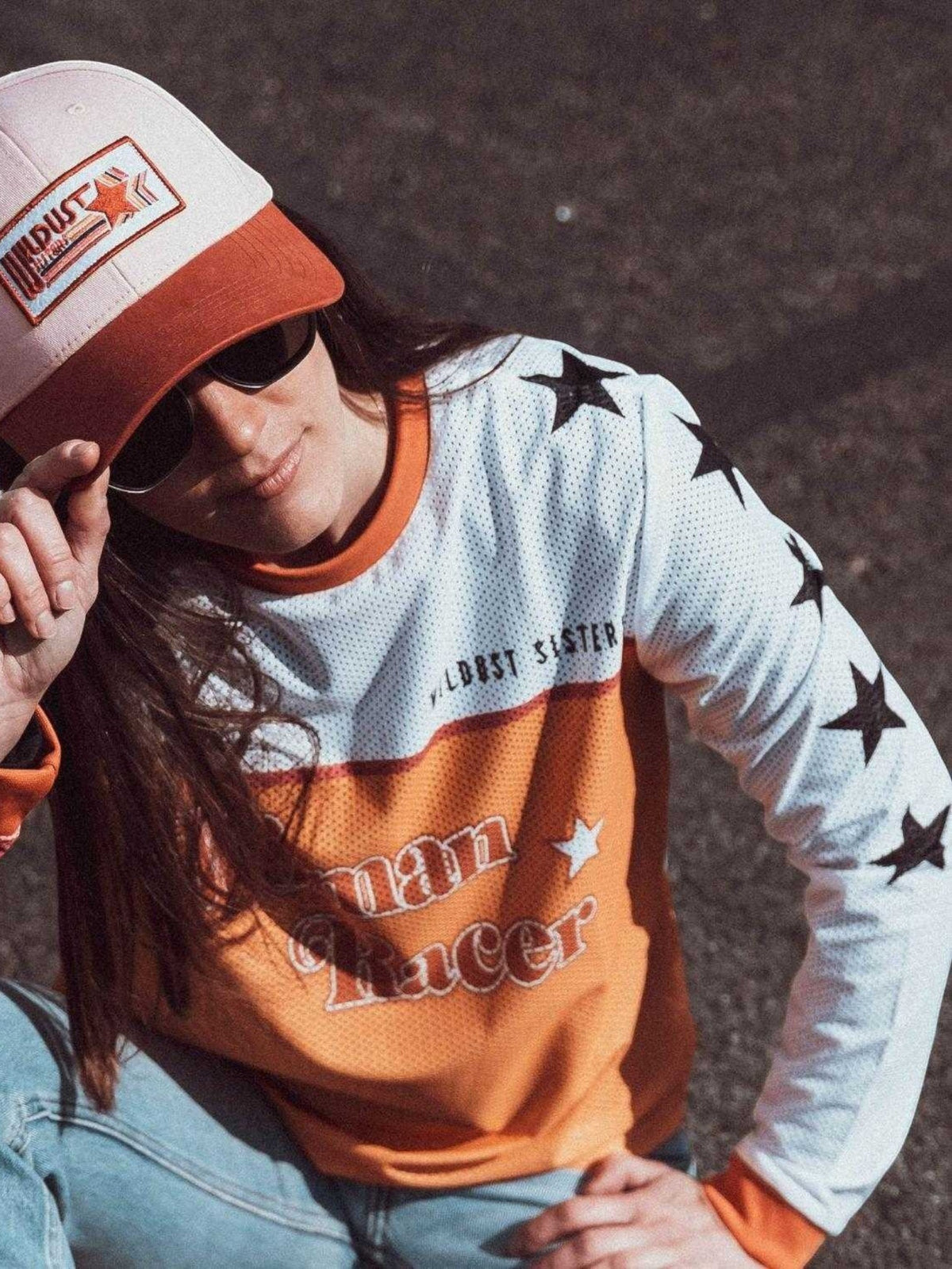 Baffle Haus Woman Racer cap in cream and orange with a vintage-style patch, worn by a woman in a matching jersey.