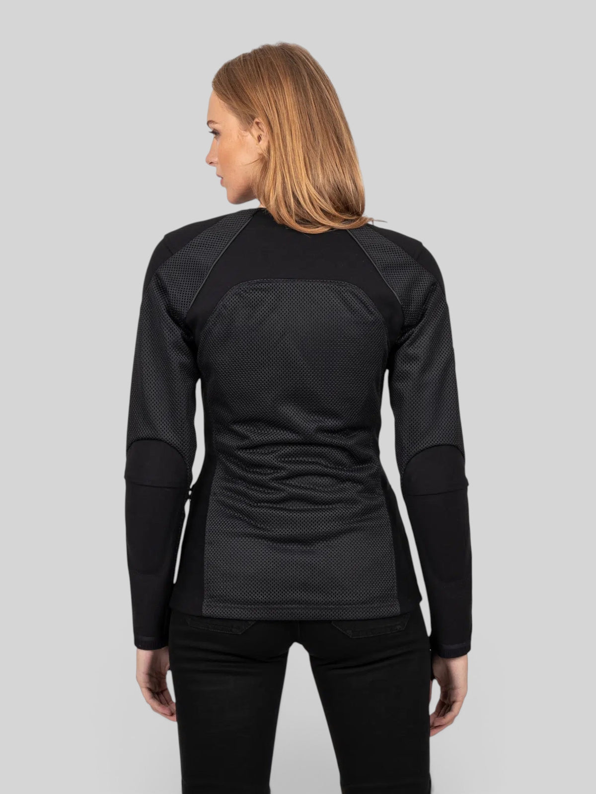 Back view of a woman wearing the black Baffle Haus Womens Urbane Pro MK3 motorcycle jacket with breathable mesh panels.