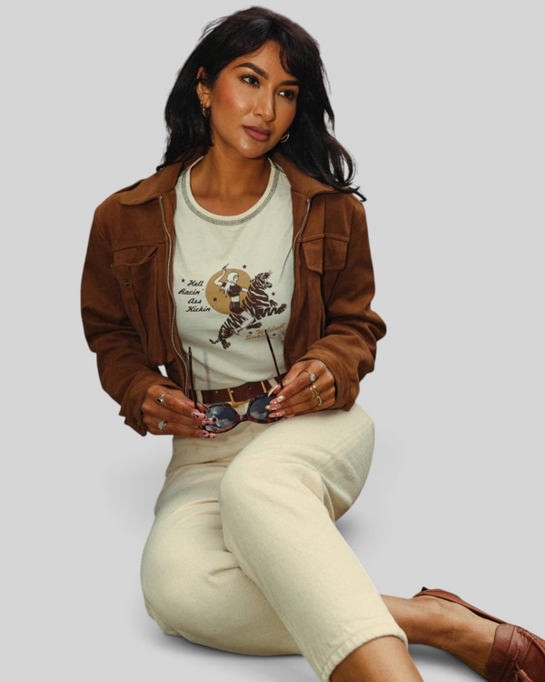 Baffle Haus white cropped cotton t-shirt with tiger rider graphic, worn under a brown suede jacket by a woman.
