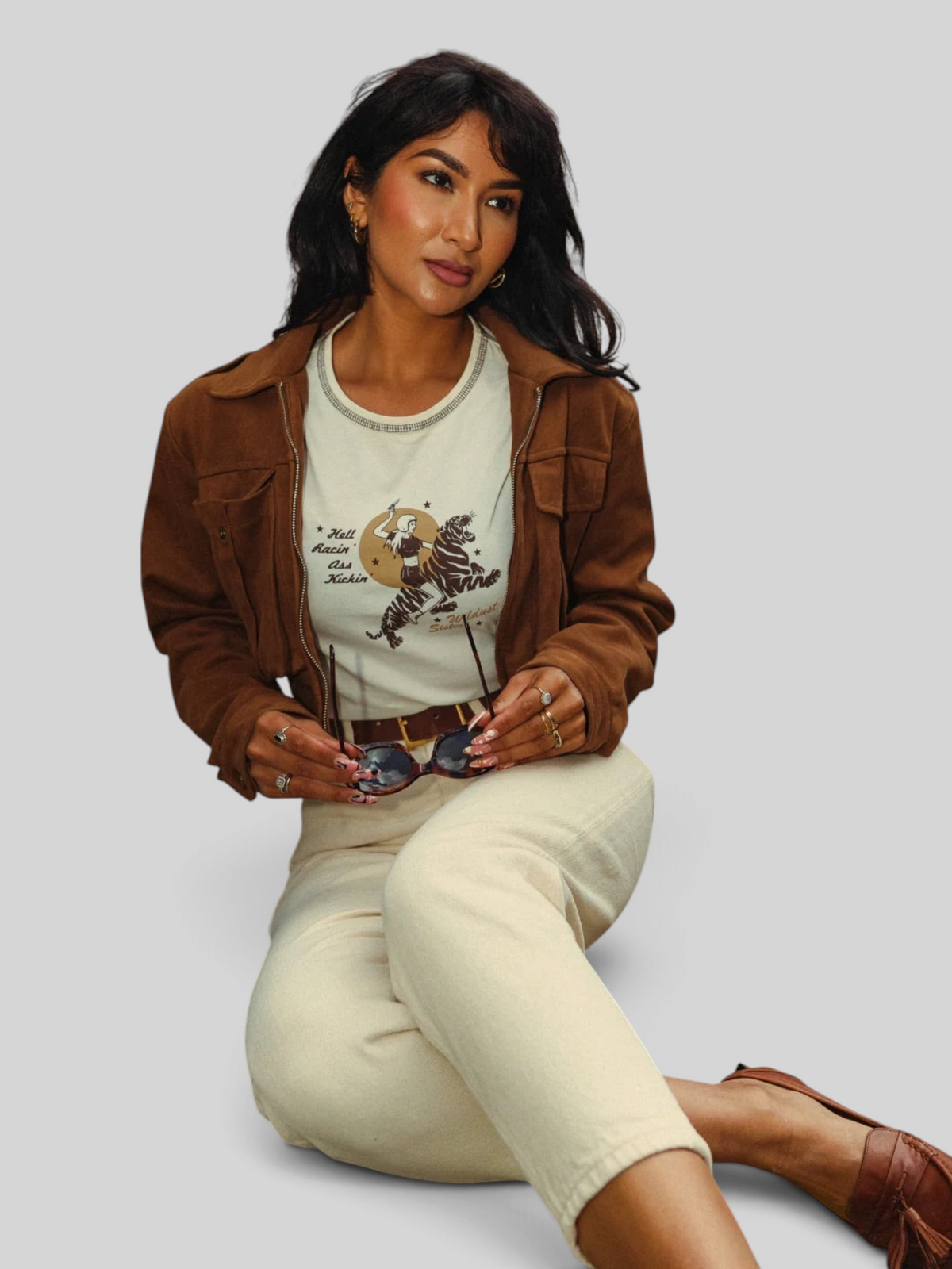 Baffle Haus white cropped cotton t-shirt with tiger rider graphic, worn under a brown suede jacket by a woman.