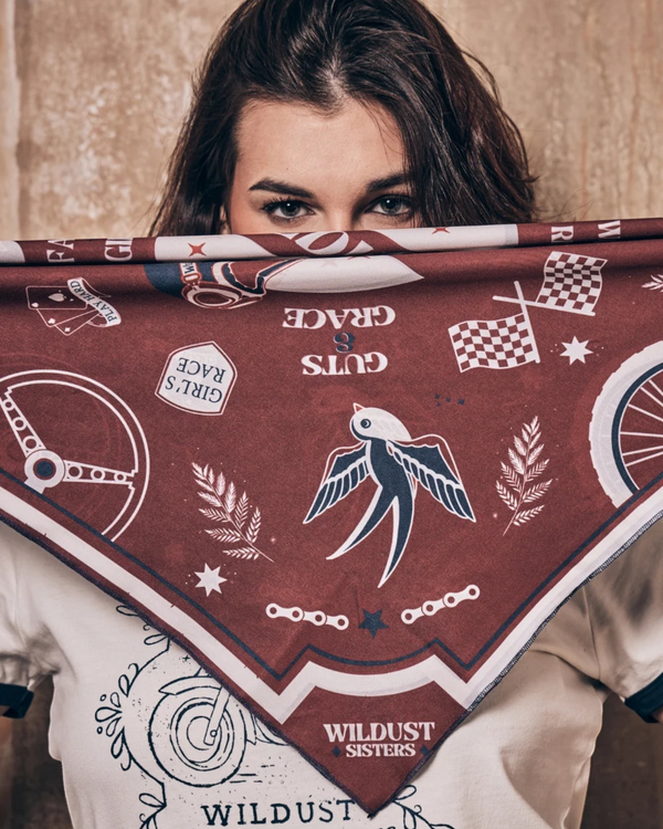 Baffle Haus Victory motorcycle scarf in terracotta and blue with retro racing graphics held over a woman's face