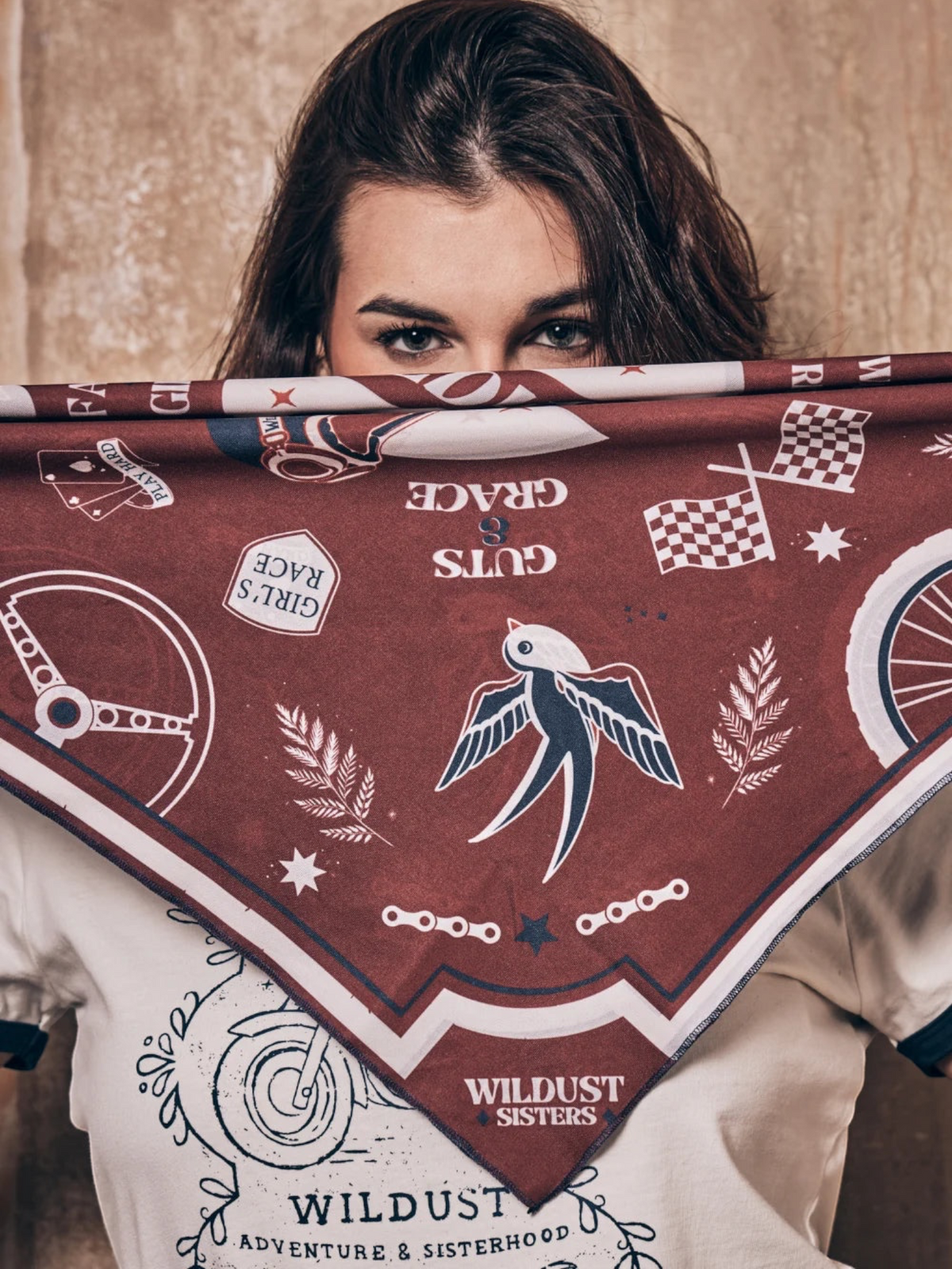 Baffle Haus Victory motorcycle scarf in terracotta and blue with retro racing graphics held over a woman's face