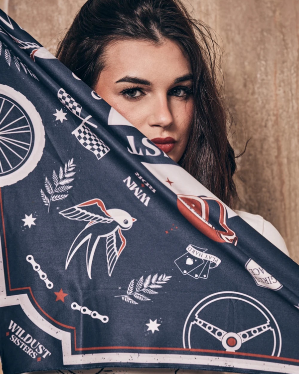 Baffle Haus Victory motorcycle scarf in blue and terracotta with retro racing prints held by a woman