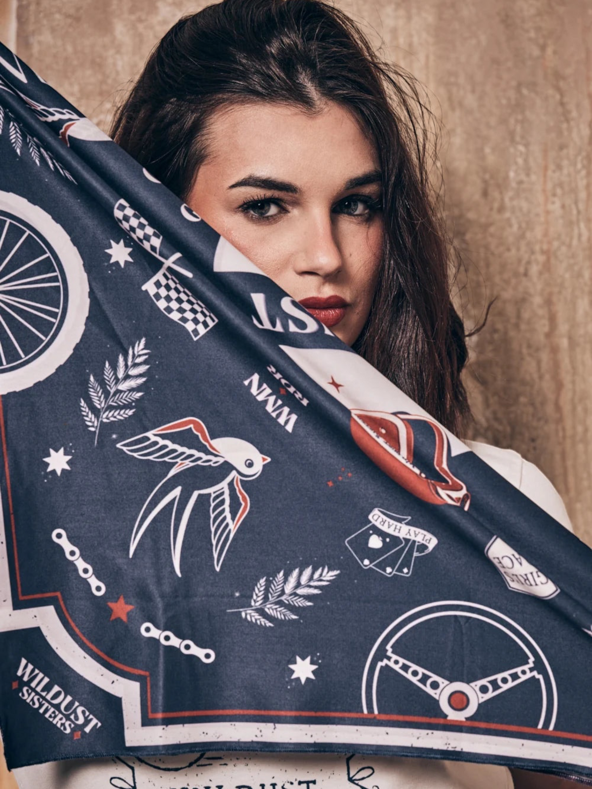 Baffle Haus Victory motorcycle scarf in blue and terracotta with retro racing prints held by a woman