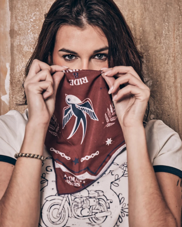 Baffle Haus Victory motorcycle scarf in terracotta and blue with swallow print worn as a face covering by a woman