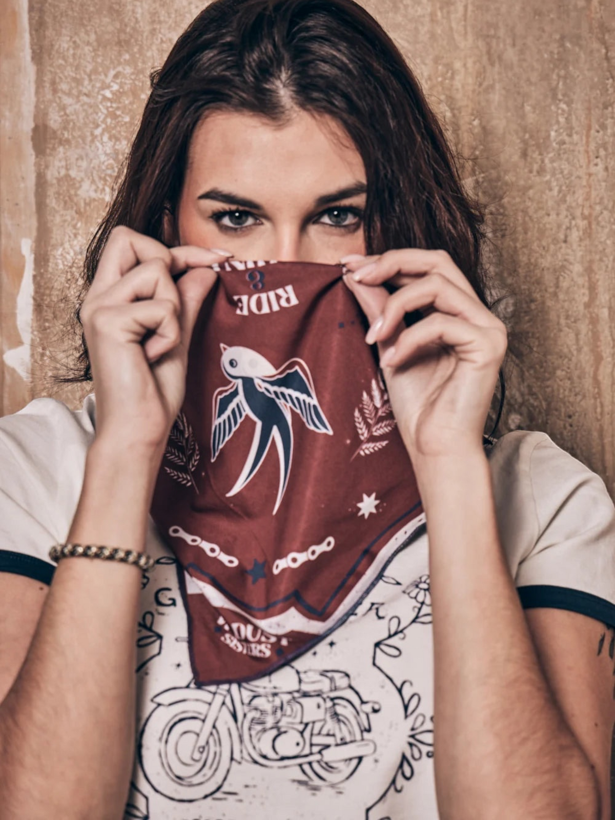 Baffle Haus Victory motorcycle scarf in terracotta and blue with swallow print worn as a face covering by a woman