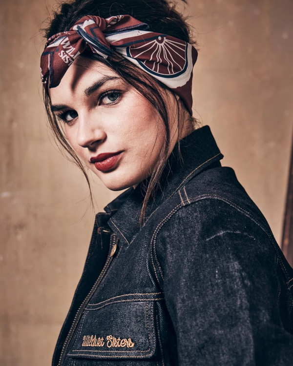 Baffle Haus Victory motorcycle scarf worn as a headscarf by a woman in a denim jacket with retro racing print