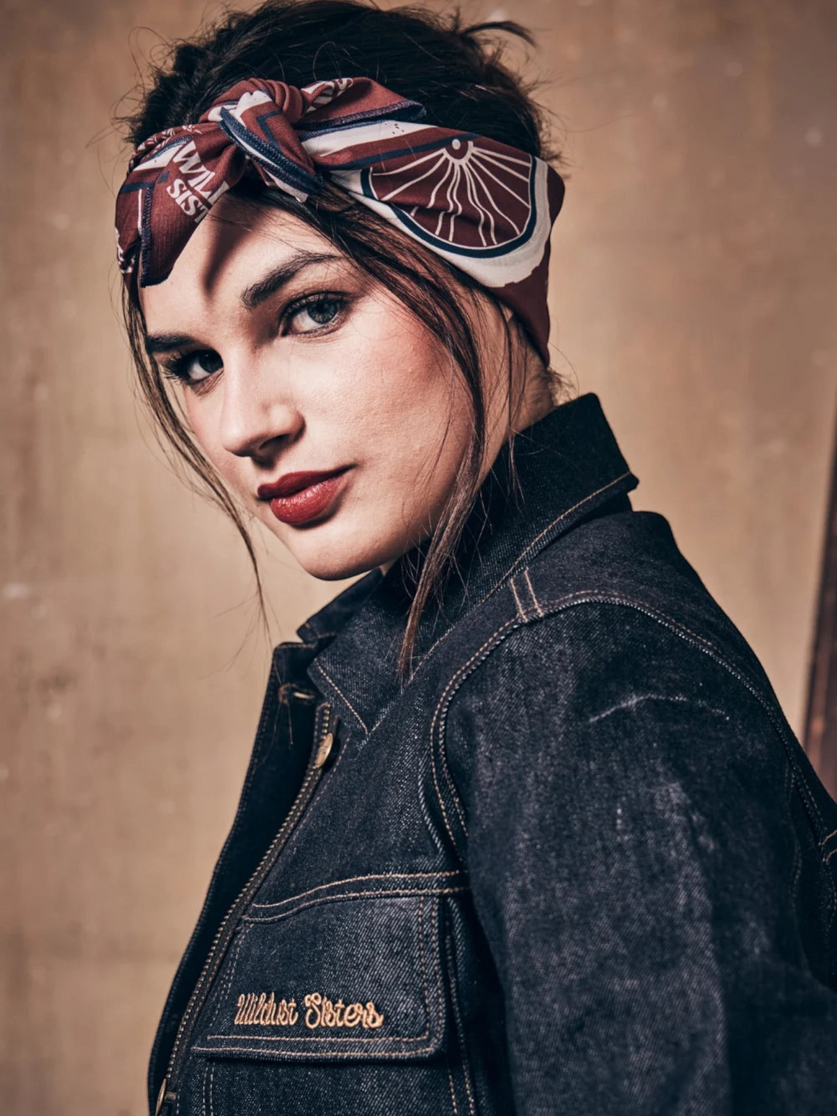 Baffle Haus Victory motorcycle scarf worn as a headscarf by a woman in a denim jacket with retro racing print