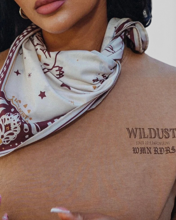 Baffle Haus Untamed Tee in khaki cotton with chest graphic, styled with a patterned neck scarf on a woman.