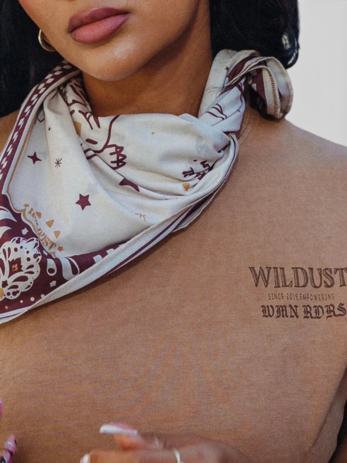 Baffle Haus Untamed Tee in khaki cotton with chest graphic, styled with a patterned neck scarf on a woman.