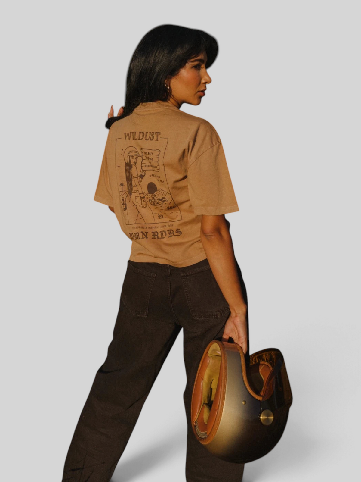Baffle Haus khaki 100% cotton cropped T-shirt with back graphic print, worn by a woman holding a vintage helmet.